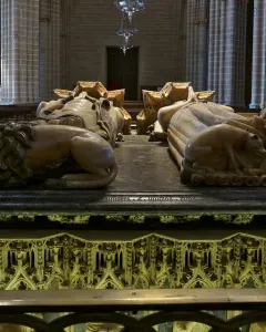 Tomb of Charles III and Eleanor with recumbent stone effigies, a lion at one figure\'s feet and two dogs at the other\'s, in a Gothic cathedral interior.