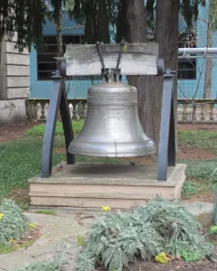 The Liberty Bell displayed on a wooden platform with a dark metal frame, surrounded by trees and ground cover.