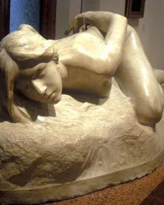 Malgré Tout, a light-colored stone sculpture of a reclining nude female figure on a rough base with the inscription \