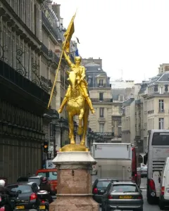 Golden equestrian statue of Joan of Arc in armor holding a flag-topped staff on a stone pedestal.