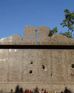 Granite Monument to Victims of the Wola Massacre with engraved Polish text and memorial candles at the base.