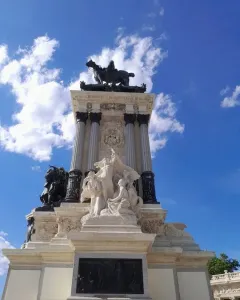 Alfonso XII Monument with a dark equestrian statue atop a multi-tiered marble base under a blue sky.