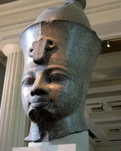 Colossal granite head of Amenhotep III displayed on a white pedestal in a museum