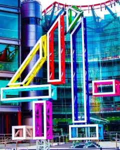 Big 4 sculpture in bright colours stands in front of a modern glass-and-steel building.