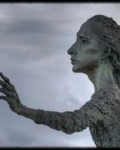 La madre del emigrante bronze statue of a woman standing barefoot with one arm outstretched in a plaza