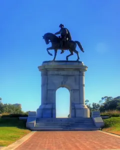 Sam Houston Statue on a stone archway with a rider on horseback above a grassy knoll and brick walkway.