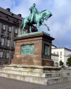 Frederick VII equestrian statue on a tall stone pedestal in a city square.