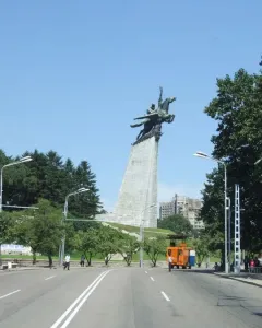 The Chollima Statue rises above a multi-lane road in Pyongyang, with trees, streetlights, and buildings in the background.
