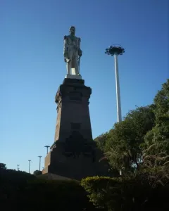 Monument to General Carlos M. de Alvear on a dark pedestal, with a tall white pole and trees beside it.