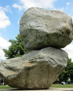 Rock on Top of Another Rock stacked on a grassy lawn with trees and people in the background