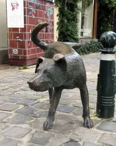 Zinneke Pis bronze dog sculpture on a cobblestone street beside a dark green bollard.