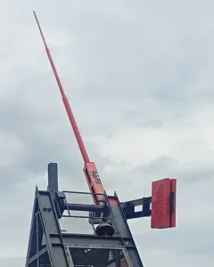 Prague Metronome mechanism with a red arm and counterweight against a cloudy sky.