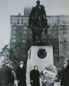 Simón Bolívar equestrian statue on a stone pedestal with men gathered below and a floral wreath at its base.