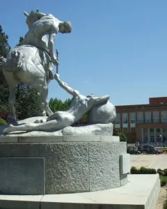 The Torch Bearers monument shows a nude rider on horseback passing a torch to a prone figure on a circular pedestal.
