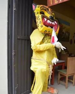 Mannequin wearing a yellow and black spotted jaguar mask, yellow jumpsuit, and white gloves, holding a small red, white, and green banner.