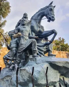 The Statue of Saladin, a bronze equestrian monument with two armed figures beside it, set against stone walls and trees.