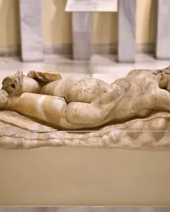 Ancient marble Sleeping Maenad reclining on a pedestal in a museum display.