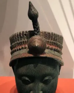 Bronze Head from Ife with fine vertical facial striations, closed eyes, and an elaborate headdress.
