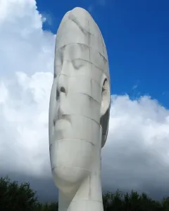 The Dream sculpture by Jaume Plensa, a tall white head and neck with closed eyes, against a blue sky with clouds.