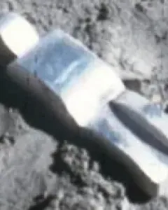 Fallen Astronaut figure lying on a textured grey surface, casting a sharp shadow.