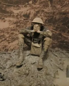 Man in the mud sculpture of a soldier sitting with hands covering his face in muddy terrain.