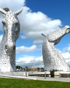 The Kelpies horse head sculptures beside water under a blue sky with clouds.