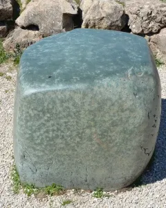 Hattusa Green Stone resting on light gravel beside a rough stone wall and grass