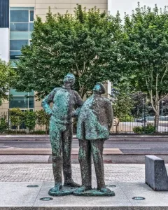 Two Working Men sculpture showing two weathered bronze figures standing side by side on a stone plinth, both looking upward to the left.