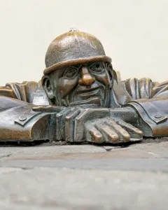 Čumil, a bronze man emerging from a street opening with his hands resting on the rim
