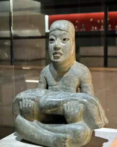 Las Limas Figurine showing a seated grey-green stone figure holding a smaller figure across its lap.