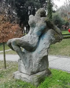 Güzel İstanbul sculpture showing a gray, reclined stone figure in a grassy park near a paved path.