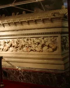 Alexander Sarcophagus with relief carvings, displayed in a glass case with a gold-chain barrier.