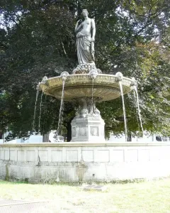 A classical draped female statue stands atop the Diana Fountain as water flows into a stone basin, with trees in the background.