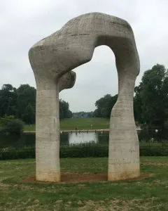 Henry Moore\'s The Arch stands on grass, framing water and distant trees under an overcast sky.