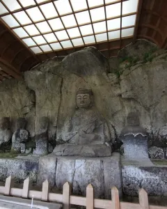 Usuki Stone Buddhas carved into a rock cliff beneath a protective wooden shelter with a fenced viewing area.