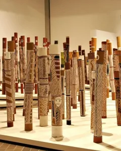Aboriginal Memorial sculpture made up of numerous decorated wooden poles standing upright on a light-colored platform.