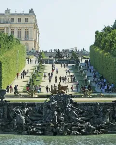 Neptune Fountain in Versailles with mythological sculptures and cascading water, set before a formal garden path leading toward the palace.