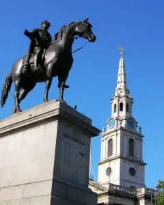 The Equestrian Statue of George IV silhouetted on its pedestal against a blue sky, with a church steeple nearby.