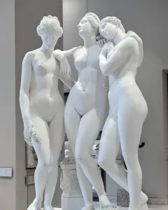 The Three Graces, a white marble sculpture of three female figures in a museum gallery.
