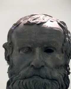 The Porticello Head bronze sculpture of an older man with a wavy beard and hollow eyes on a pedestal.