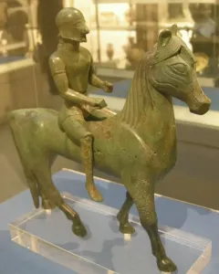 Armento Rider bronze statuette of a helmeted rider on a horse, shown on a clear stand.