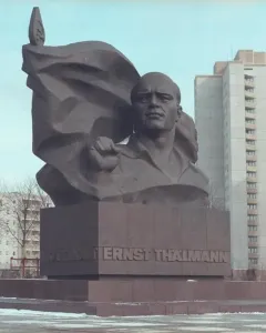 Ernst Thälmann Memorial bronze bust with a clenched fist and banner-like sculpture on a pedestal in a snowy urban setting.