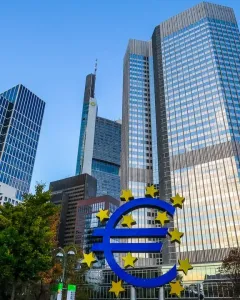 Blue Euro sculpture with yellow stars in front of modern glass skyscrapers.