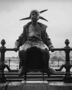 The Little Princess statue sits on a decorative railing, shown in black and white with a distant landscape behind it.