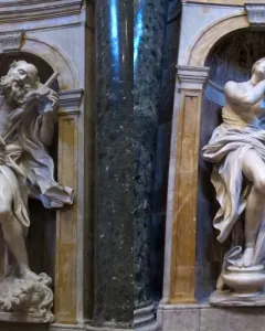 Saints Jerome and Mary Magdalen marble statues in arched niches with dark columns, showing Jerome holding a cross and Magdalen gazing upward.