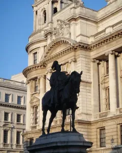 The Duke of Cambridge equestrian statue silhouetted against a grand stone building and blue sky.