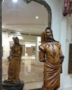 Mephistopheles and Margaretta wooden sculpture showing a bearded male figure, with the female side visible in the mirror behind it.