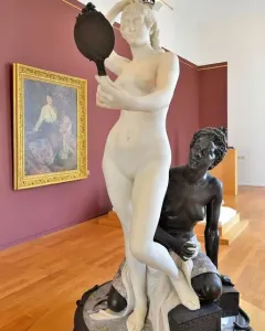 Le Miroir sculpture showing a white marble nude woman holding a hand mirror above a kneeling bronze figure on a decorative base.