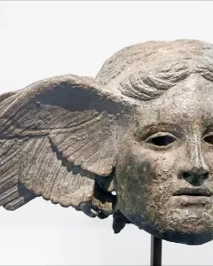 Bronze head of Hypnos with a green patina, serene face, and a wing extending from one side.