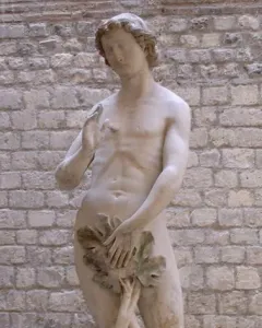 Stone statue of Adam standing nude with a leaf covering his groin and one hand raised.